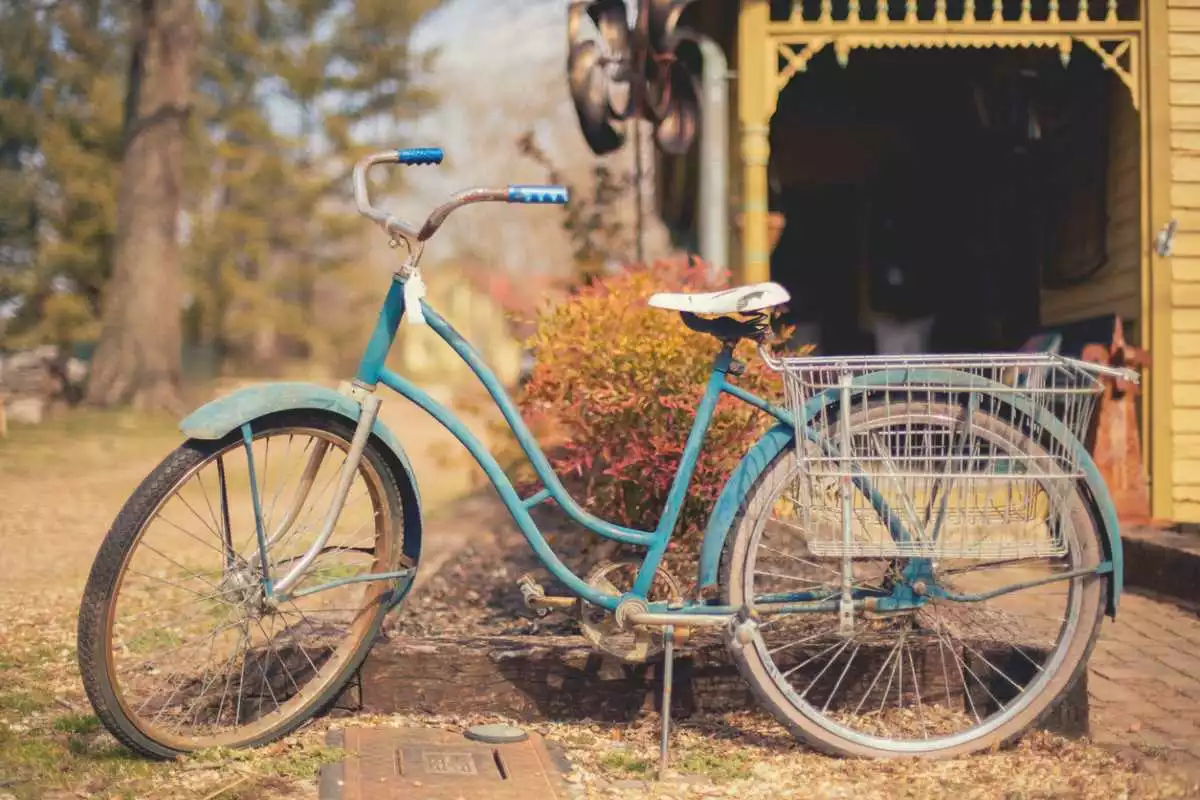 An antique bicycle rests along an old home in a rural setting.