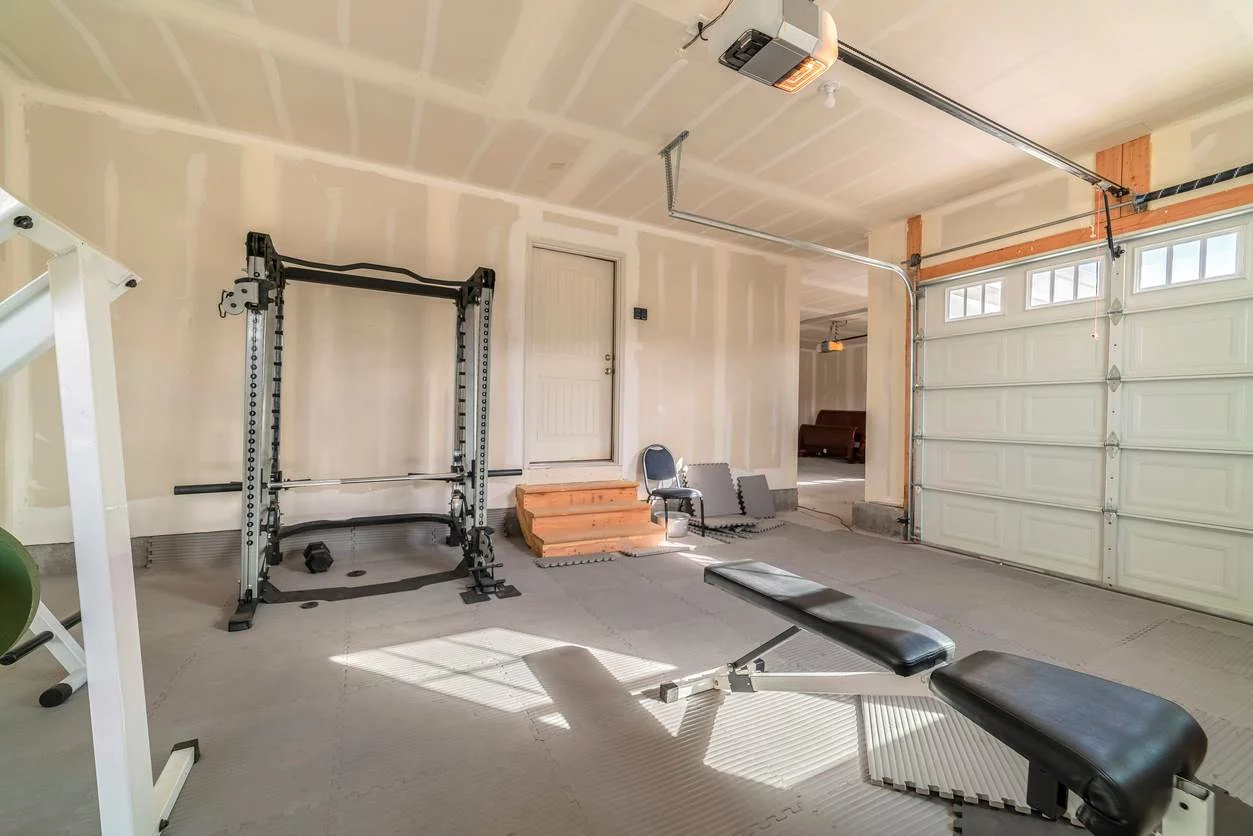 A garage gym complete with a bench, squat rack, and foam tiles