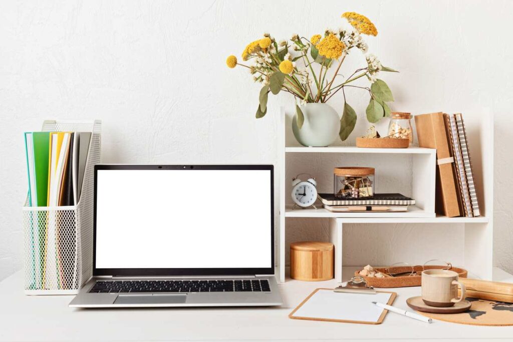 A tidy desk with a blank computer, decorations, a desk organizer, shelves, and office supplies.